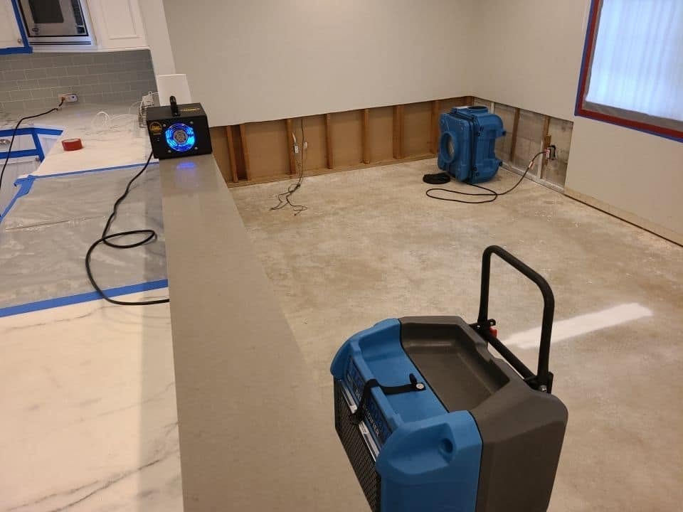 Drying equipment running in water-damaged room with exposed wall framing