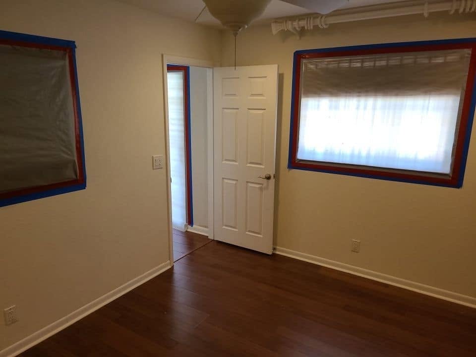 Restored bedroom with blue and red tape containment barriers on windows after water damage remediation