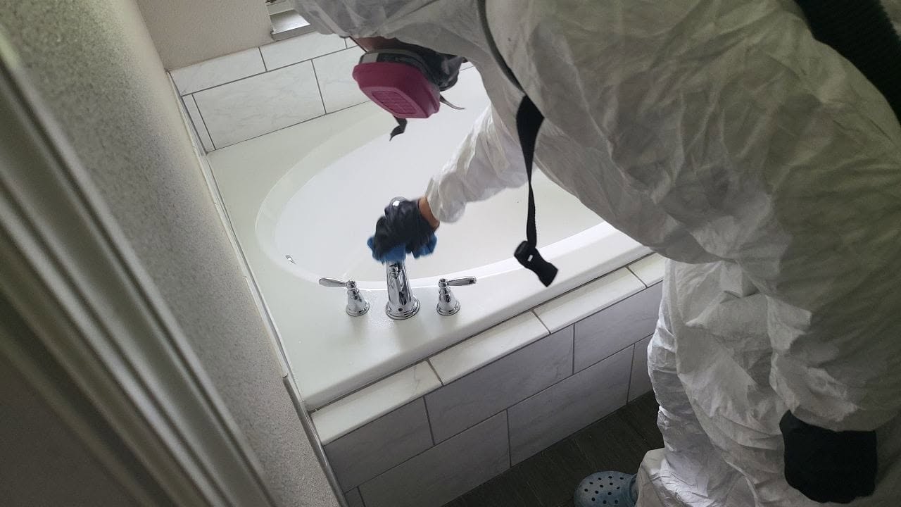 Mold remediation technician in protective suit cleaning bathtub during bathroom mold remediation