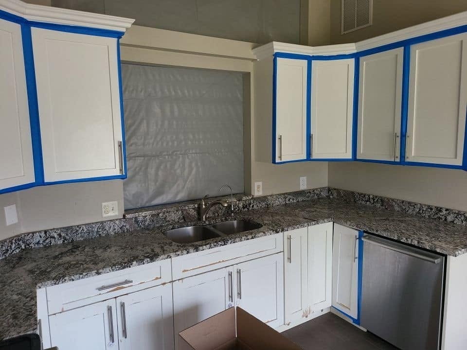 Kitchen with blue tape containment barriers and plastic sheeting on windows during mold remediation