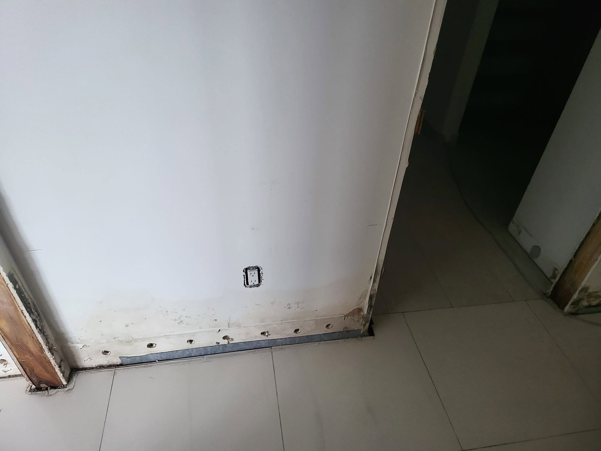 Water-damaged wall base with mold staining and drywall cutout showing moisture damage at floor level