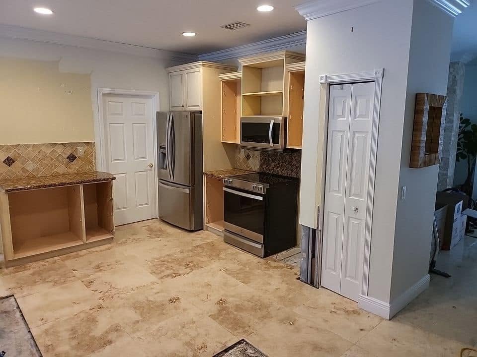 Kitchen with open cabinets and water-stained floor tiles during water damage assessment