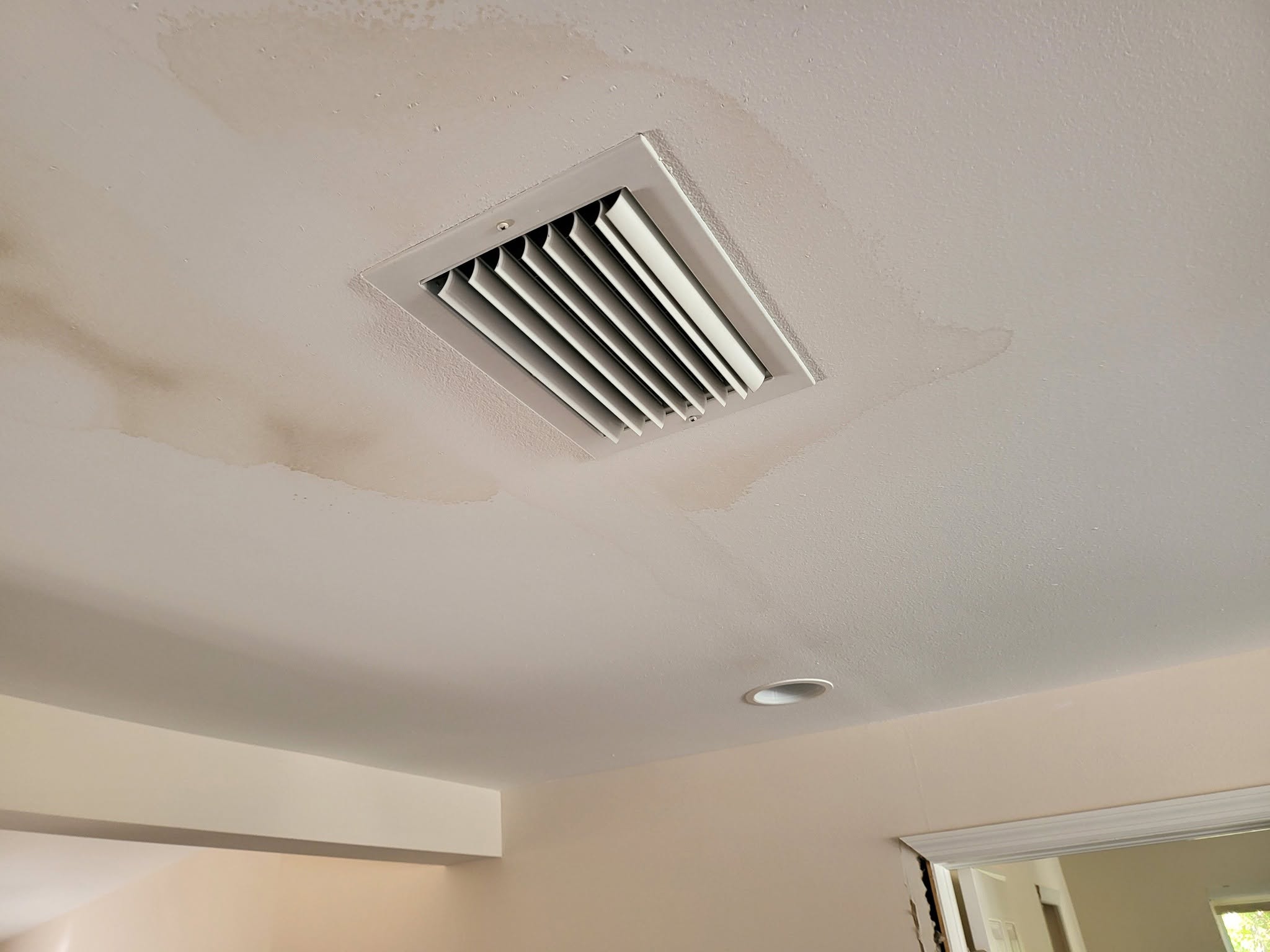 Water stains and moisture damage spreading across ceiling around HVAC vent register